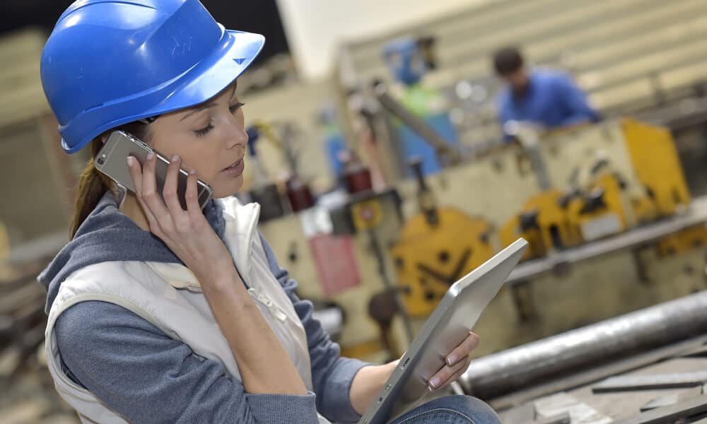 woman on manufacturing floor looking at tablet and talking on phone