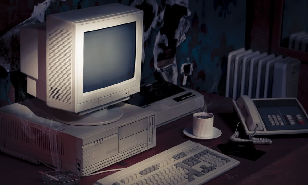 Outdated computers sitting in a dark work station with a coffee cup to the side.