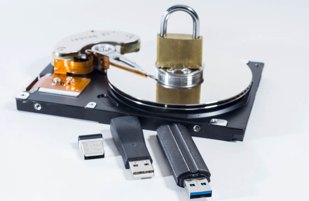 Image of hard drive with USB sticks and a lock on top representing encrypting data at rest.