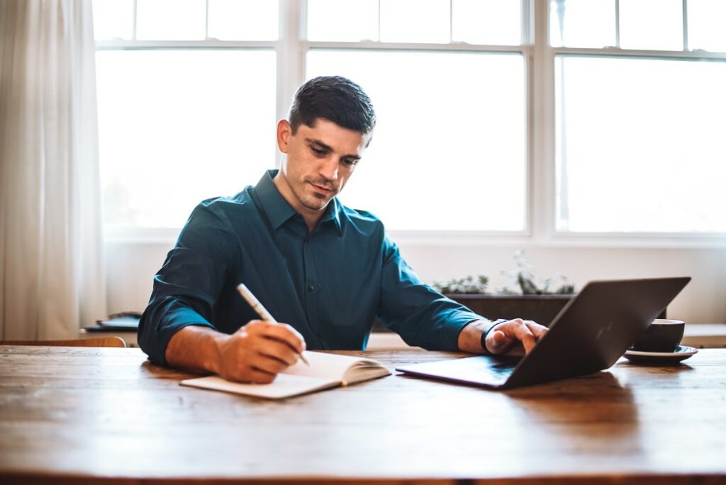 man working on laptop at desk with notepad