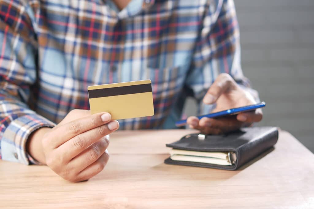 man holding credit card and phone, making a purchase on a website that has met pci compliance requirements