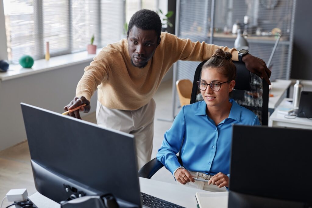 coworkers in office discussing tasks on computer